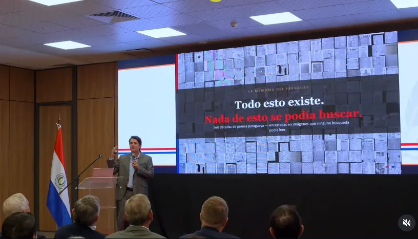 The launch presentation in Asunción: a speaker at a lectern beside Paraguay’s flag, in front of a slide reading “Todo esto existe. Nada de esto se podía buscar.”